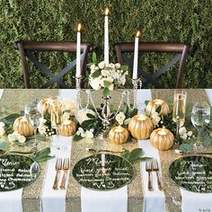 the table is set with place settings and gold pumpkins, greenery, and candles