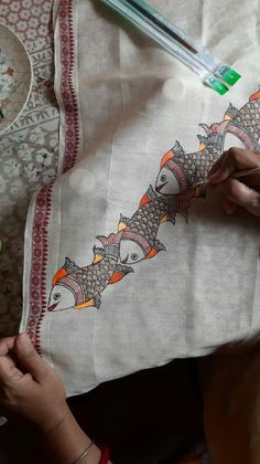 a woman is stitching a pillow with fish on it and another person is holding something in their hand