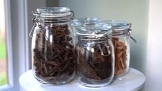 three glass jars filled with different types of food on top of a white shelf next to a window