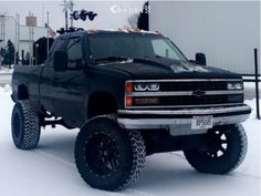 a large black truck is parked in the snow near a building and traffic light pole