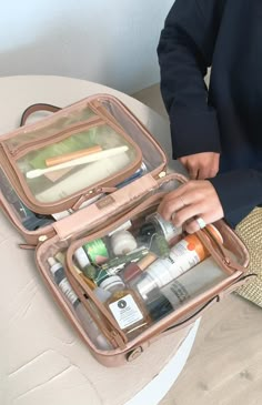 a woman sitting on a stool holding an open suitcase filled with cosmetics and other items