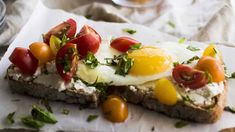 two pieces of bread with eggs and tomatoes on top, sitting on a napkin next to a glass of water