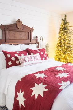 a bed with red and white comforter next to a christmas tree in a bedroom