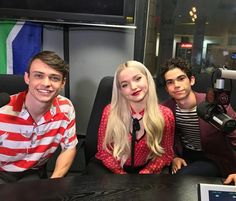 three people sitting at a table with microphones in front of them and a laptop on the desk