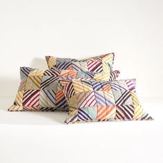 two decorative pillows sitting next to each other on a white surface, one is multicolored