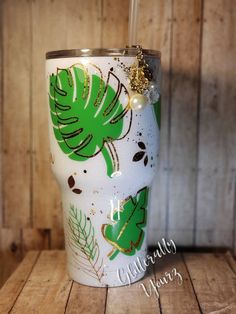 a white cup with green leaves and pearls on the lid sitting on a wooden table