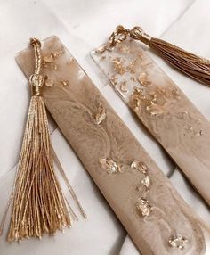 two long beige and gold tassels on a white surface