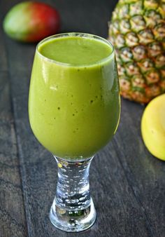 a glass filled with green smoothie next to some fruit