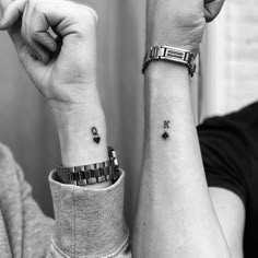 two people with matching wrist tattoos holding their hands up in the air and looking at each other