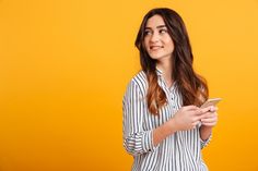 a woman in striped shirt looking at her cell phone while standing against an orange background