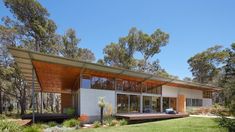 a modern house in the middle of some trees and grass with an open patio area