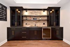 an empty kitchen with black cabinets and wood floors