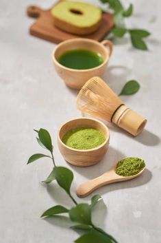 three wooden spoons filled with green tea next to some leaves on a white surface