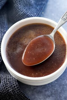 a spoon full of brown liquid sitting in a white bowl on top of a blue towel