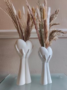 two white vases with plants in them sitting on a glass table top next to each other