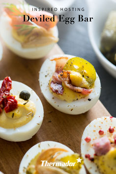 deviled eggs with different toppings are on a wooden board next to other dishes