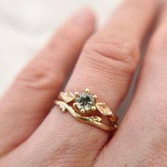 "Handcrafted from a delicate budded twig, the Flora Solitaire Band is adorned with thyme leaves and features a mint green Montana Sapphire in a 6-prong setting.  100% recycled gold  100% ethically-sourced Montana Sapphire Every single ring in my collection is designed, sculpted and produced entirely by hand. I never use computers and I never use \"off-the-shelf\" designs that you see in so many jewelry stores. Each ring begins by casting an actual twig or piece of bark; its natural, imperfectly Leaf Engagement Ring Nature, Engagement Rings Organic, Stacked Engagement And Wedding Rings, Contour Ring, Green Montana, Nature Engagement Ring, Solitaire Bands, Montana Sapphire Ring, Sapphire Solitaire Ring