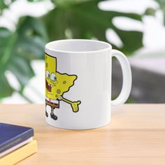 a white coffee mug with a cartoon character on it sitting on a table next to a book