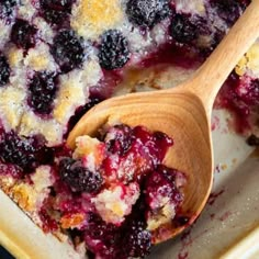 a close up of a casserole dish with blueberries on it and a wooden spoon