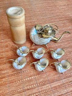 a tea pot and eight silver cups on a rug next to a cup with saucer