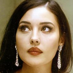 a close up of a woman with long hair and large earrings on her head, looking at the camera