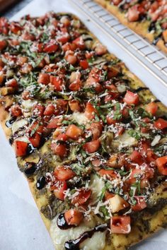 two pizzas with tomatoes, olives and parmesan cheese on them sitting on a cooling rack