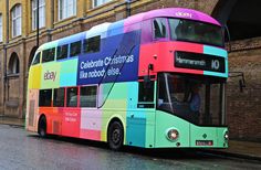 a multicolored double decker bus parked in front of a building on the street