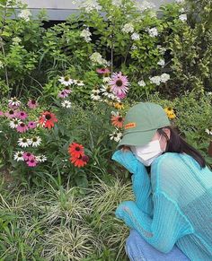 a woman wearing a face mask sitting in the middle of a garden filled with flowers