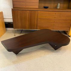 a wooden table sitting on top of a white floor next to a dresser and bookcase