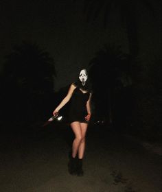 a woman wearing a mask and holding a tennis racquet in the dark with palm trees behind her