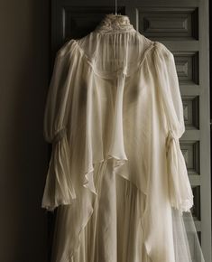 a white dress hanging on a door with sheer fabric and ruffles around it