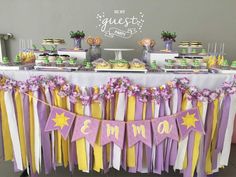 a table topped with cake and desserts covered in purple, yellow and white ribbons