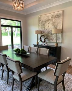 a dining room table and chairs in front of a large window with a painting on the wall