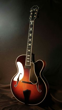 an acoustic guitar sitting on top of a black cloth covered surface with light coming from behind it