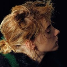 a woman with blonde hair wearing gold hoop earrings and black fur coat looking off to the side