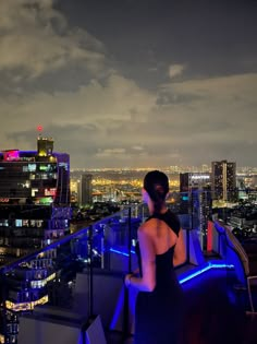 a woman standing on top of a building looking out over the city at night time