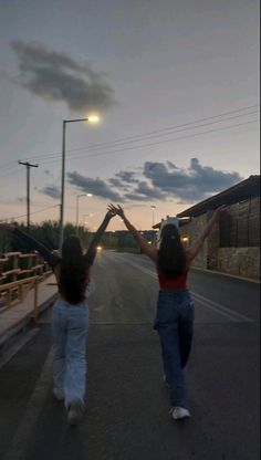 two women are walking down the street holding their hands in the air and one is raising her arms up