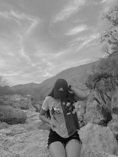 black and white photograph of a woman in shorts sitting on rocks with mountains in the background