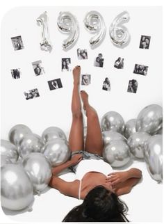 a woman laying on the ground surrounded by silver balloons and photos that spell out her birth year