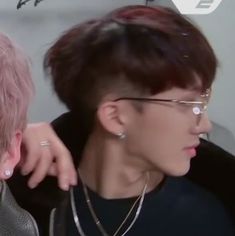 two people with pink hair and glasses are looking at each other's eyes while one person has his hand on the shoulder of another