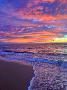 an ocean beach with waves coming in to the shore and colorful clouds above it at sunset