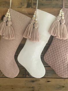 three stockings with tassels hanging from them on a wooden wall next to a white stocking