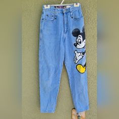 a pair of blue jeans with mickey mouse on them hanging from a hook in front of a wall