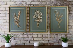 three framed flowers on a brick wall next to two potted plants in vases