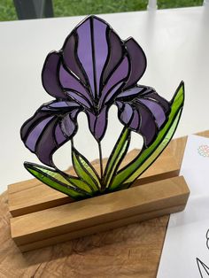 a stained glass flower sitting on top of a wooden stand next to a piece of paper