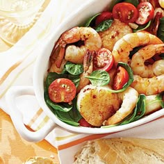 shrimp salad with spinach and tomatoes in a white bowl on top of a table