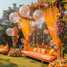 an outdoor seating area with balloons and flowers on the grass, surrounded by orange drapes