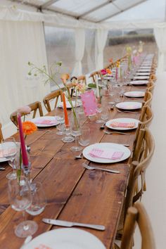 a long wooden table with white plates and pink napkins is set up for a party