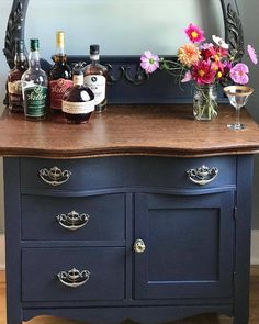 a blue dresser with flowers and liquor bottles on it's top, in front of a mirror