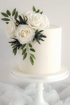 there is a white cake with flowers on the top and green leaves on the bottom